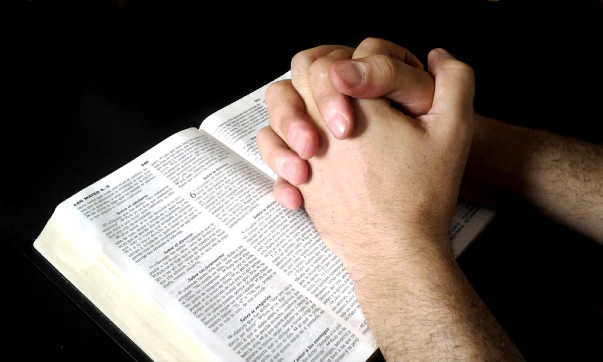 A pair of hands folded in prayer over an open Bible